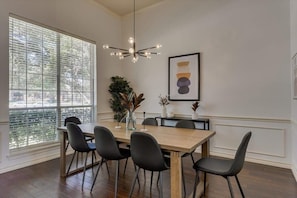 A dining area with a wooden table, black chairs, a chandelier, and a window with blinds. - Spacious & Cozy Texas Gem With Private Pool (Plano)