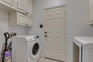 A laundry room with a washing machine, a dryer, and a vacuum cleaner. - Spacious & Cozy Texas Gem With Private Pool (Plano)