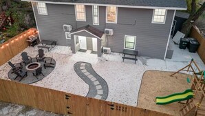 Een tweelaags huis met een overdekte patio, een vuurplaats en een speelconstructie voor kinderen.
