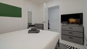 Een slaapkamer met een bed, een televisie, een dressoir en een deur naar een andere kamer.
