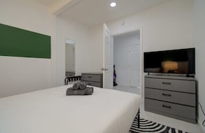 Ein Schlafzimmer mit einem Bett, einem Fernseher, einer Kommode und einer Tür zu einem anderen Raum.
