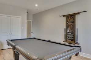 A pool table in a room with a door and a wall-mounted shelf with decorative items. - Vibrant Texas Escape 5br, Pool & Hot Tub (Rowlett)
