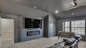 A spacious living room with a large flat-screen TV, a foosball table, and a leather recliner. - 5BR Oasis w/ Pool Steps From Lake Ray hubbard (Rowlett)