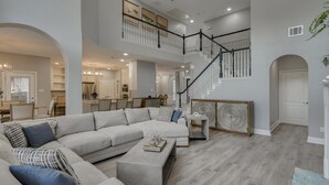A spacious living area with a large sectional sofa, a coffee table, and a staircase leading to an upper level. - 5BR Oasis w/ Pool Steps From Lake Ray hubbard (Rowlett)