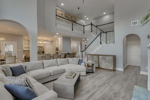 A spacious living area with a large sectional sofa, a coffee table, and a staircase leading to an upper level. - 5BR Oasis w/ Pool Steps From Lake Ray hubbard (Rowlett)