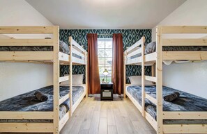 Ein Zimmer mit zwei Etagenbetten, einem Vorhangfenster und einem kleinen Tisch mit Lampe.