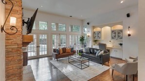 A spacious living room with a stone accent wall, a large window, a fireplace, and a modern fireplace mantel. - Dallas Gem 5 Bedrooms Home With Pool, Game Room (Dallas)
