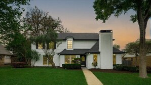 A two-story house with a front entrance, a visible garage, and a well-maintained lawn. - Perfect Getaway Home w 5 Bedrooms & Backyard Oasis (Plano)
