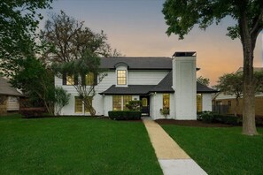 A two-story house with a front entrance, a visible garage, and a well-maintained lawn. - Perfect Getaway Home w 5 Bedrooms & Backyard Oasis (Plano)