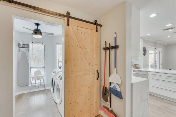 A laundry room with a washing machine, a drying rack, and a broom leaning against the wall. - Perfect Getaway Home w 5 Bedrooms & Backyard Oasis (Plano)
