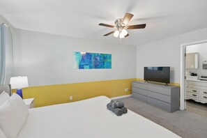 A hotel room with a bed, a ceiling fan, a TV, a dresser, and a painting on the wall. - Modern & Chic 4-bd/2-ba Pool, Hot Tub, BBQ Grill (Carrollton)