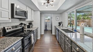 A modern kitchen with granite countertops, stainless steel appliances, and a view to a backyard pool. - Modern & Chic 4-bd/2-ba Pool, Hot Tub, BBQ Grill (Carrollton)