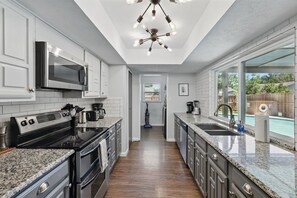 A modern kitchen with granite countertops, stainless steel appliances, and a view to a backyard pool. - Modern & Chic 4-bd/2-ba Pool, Hot Tub, BBQ Grill (Carrollton)