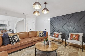 A modern living room with a brown leather sofa, a round coffee table, and a patterned rug. - 5BR w/ Backyard Paradise, Pool, Cinema, games (North Richland Hills)