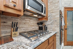 A kitchen with a stainless steel microwave, a gas stove, wooden cabinets, and a granite countertop. - Lewisville Luxe Oasis Pool, Bbq, Theater Room (Lewisville)