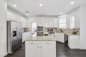 A modern kitchen with white cabinetry, stainless steel appliances, granite countertops, and a dark floor. - Luxury Home w Hot Tub Near DFW Airport (Flower Mound)