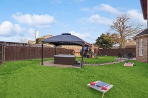 A backyard with a covered seating area, a hot tub, and a play structure. - Luxury Home w Hot Tub Near DFW Airport (Flower Mound)