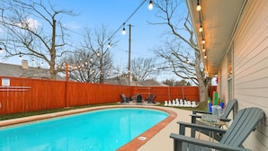 Ein Garten mit Swimmingpool, Liegestühlen und Lichterketten.