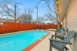 A swimming pool with a wooden fence, outdoor seating, and string lights. - Luxury Living w/ Backyard Pool Oasis (Midlothian)