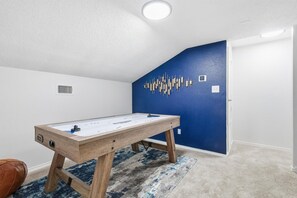 A room with a foosball table, a blue accent wall, and a patterned rug. - Luxury Living w/ Backyard Pool Oasis (Midlothian)