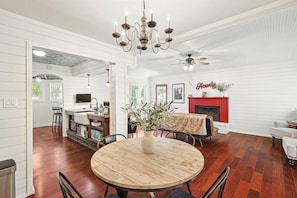A dining area with a round wooden table, chairs, a chandelier, and a fireplace. - 3BD Farmhouse Country Living - Pool, Patio, Firepit (McKinney)