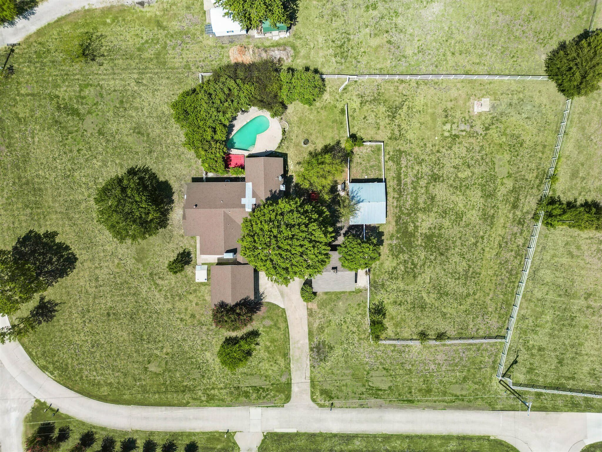 An aerial view of a residential area with a house, a swimming pool, and a fenced yard.