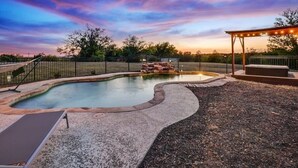 Una piscina con borde curvo, un jacuzzi y una zona de estar cubierta.