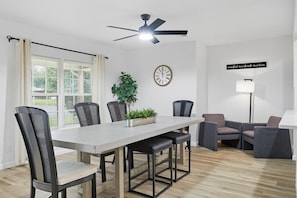 A dining area with a table, chairs, a ceiling fan, a clock, a plant, and a couch. - Inactive (Sherman)