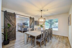 A dining area with a wooden table and chairs, a chandelier, and a sliding barn door. - Stunning Modern Dream Home w Pool, Grill, Foosball (Houston)
