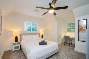 A modern bedroom with a bed, bedside lamps, a desk, and a ceiling fan. - Stunning Modern Dream Home w Pool, Grill, Foosball (Houston)