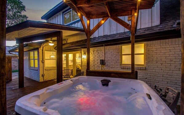 A hot tub under a wooden pergola with a brick wall and windows in the background. - Stunning Modern Dream Home w Pool, Grill, Foosball (Houston)