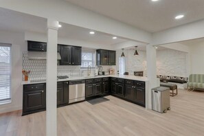 A modern kitchen with dark cabinetry, a stainless steel dishwasher, and a compact refrigerator. - Texas Designer Home With Private Hot Tub and Pool! (North Richland Hills)