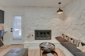A living room with a stone wall, a fireplace, a sofa, a coffee table, and a pendant light. - Texas Designer Home With Private Hot Tub and Pool! (North Richland Hills)