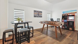 A room with a foosball table, a table with chairs, and a gaming machine. - Brand New 5bd, 4BA Luxury Vacation Home w Hot Tub (Irving)