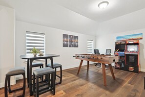 A room with a foosball table, a table with chairs, and a gaming machine. - Brand New 5bd, 4BA Luxury Vacation Home w Hot Tub (Irving)
