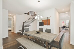 Uma sala de jantar com uma mesa de madeira, bancos, um candelabro e uma escada.