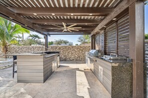 An outdoor kitchen area with a stone wall, a ceiling fan, and a grill. - Tropical Pool Paradise x 6-bd, 4-ba Luxury Living (Miami Lakes)