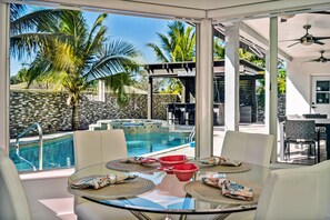A glass-enclosed dining area with a pool view, white furniture, and a stone wall. - Tropical Pool Paradise x 6-bd, 4-ba Luxury Living (Miami Lakes)
