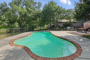 A swimming pool with a wooden deck and brick border, surrounded by trees and a fenced area. - Best of Garland Pool, Cinema Rm, BBQ (Garland)