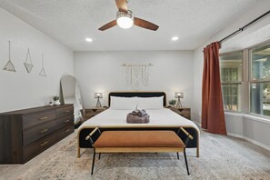 A bedroom with a bed, a ceiling fan, bedside lamps, a dresser, a window with curtains, and a wall-mounted macrame. - Best of Garland Pool, Cinema Rm, BBQ (Garland)