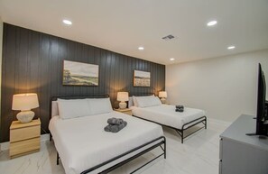 A hotel room with two beds, each with a bedside table and lamp, a flat-screen TV, and artwork on the wall. - Central Convenience x Modern Luxury - Heart of Houston (Houston)