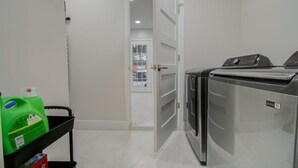 A laundry room with a washing machine, a dryer, and a cart with cleaning supplies. - Central Convenience x Modern Luxury - Heart of Houston (Houston)