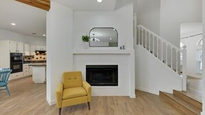 Una sala de estar moderna con chimenea, una escalera y un comedor con una silla azul.