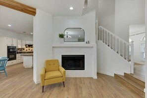 Ein modernes Wohnzimmer mit Kamin, einer Treppe und einem Essbereich mit weißen Schränken.