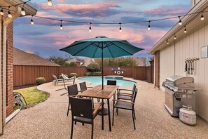 Une terrasse extérieure avec une piscine, un barbecue et des guirlandes lumineuses.