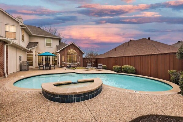 Un jardin avec une piscine, un jacuzzi et un patio couvert.
