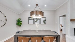 A dining area with a rectangular table, three wooden chairs, a hanging light fixture, and framed artwork on the wall. - Boho Chic Home w Backyard Paradise - Pool + Grill (North Richland Hills)