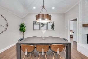 A dining area with a rectangular table, three wooden chairs, a hanging light fixture, and framed artwork on the wall. - Boho Chic Home w Backyard Paradise - Pool + Grill (North Richland Hills)