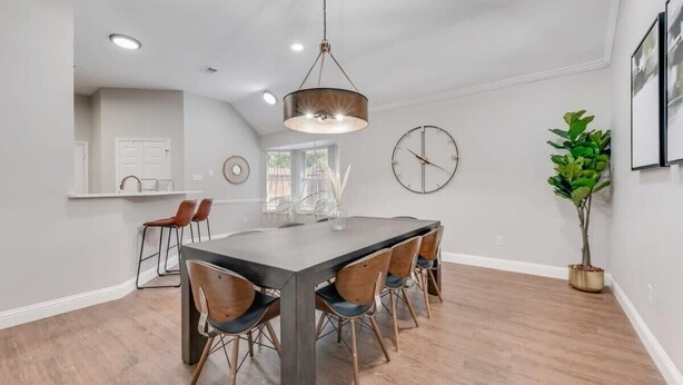 A modern kitchen with a large island, wooden chairs, and a hanging light fixture. - Boho Chic Home w Backyard Paradise - Pool + Grill (North Richland Hills)