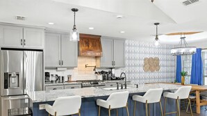 Una cocina moderna con electrodomésticos de acero inoxidable, encimera de mármol y taburetes de bar.